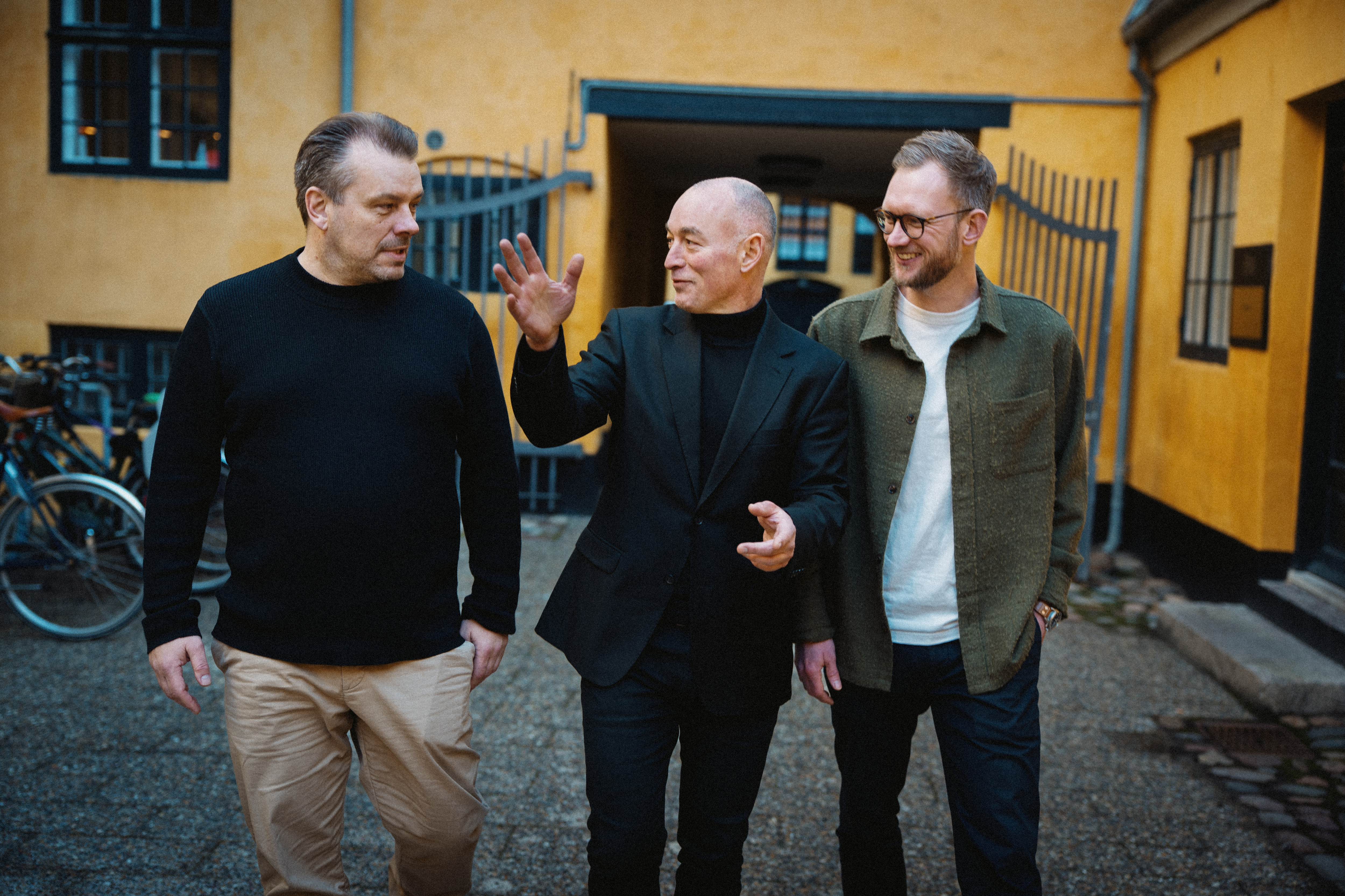 Three men in business attire walking confidently outdoors against a modern building, representing the Stella team or partners